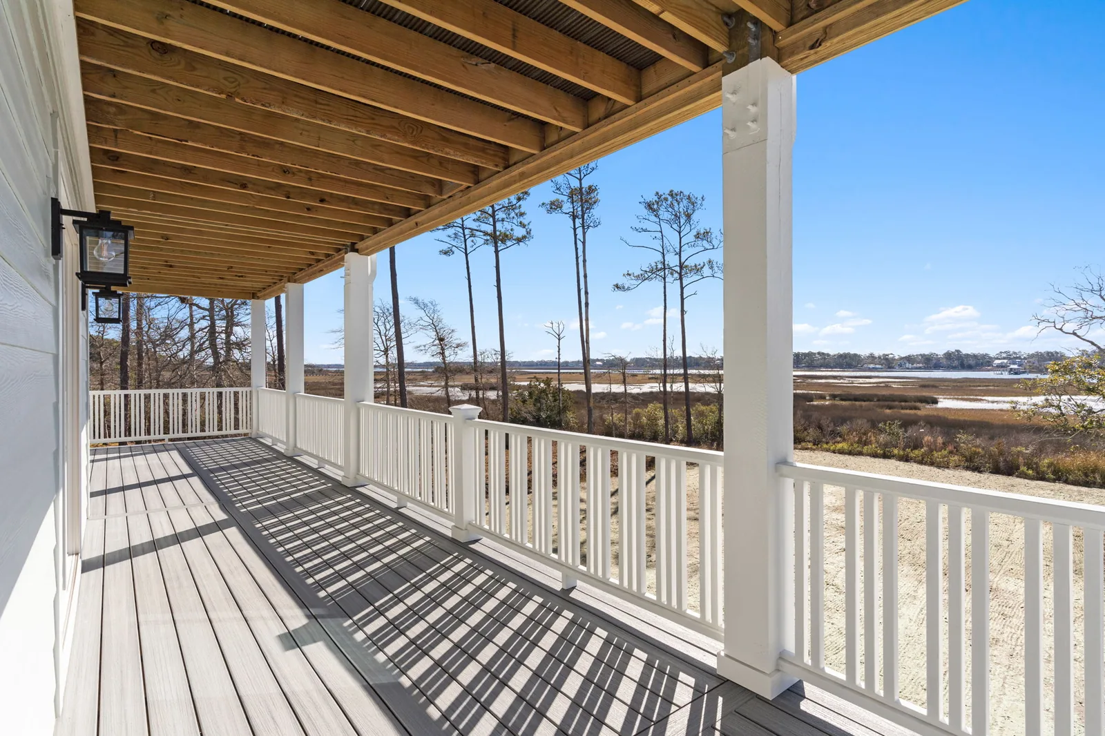 Covered deck with a wood-plank ceiling looking out over the tidal marsh at a custom beach house in Southport, NC
