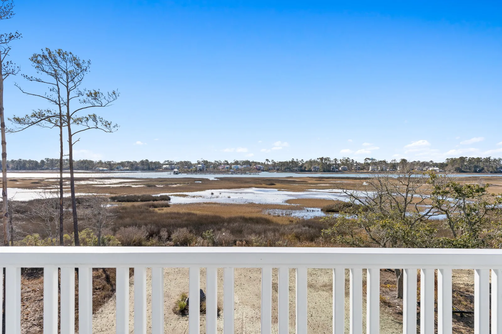 Long covered porch with railing overlooking coastal marsh grass at the Scupper Run custom home in Southport, NC